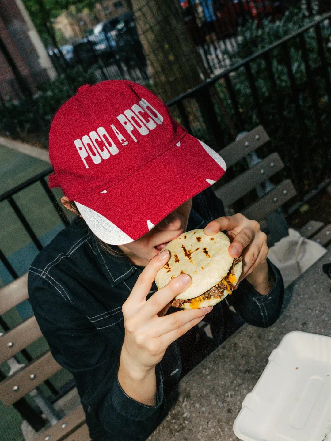 person wearing Poco A Poco hat eating an Arepa